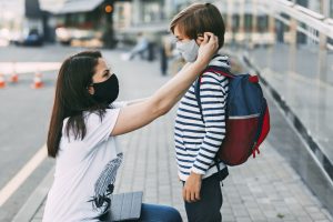 Picture of a mother adjusting her son's face mask before he goes to school.